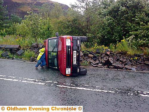 A recovery driver checks out the overturned Land Rover on Ripponden Road near the badly damaged wall. 