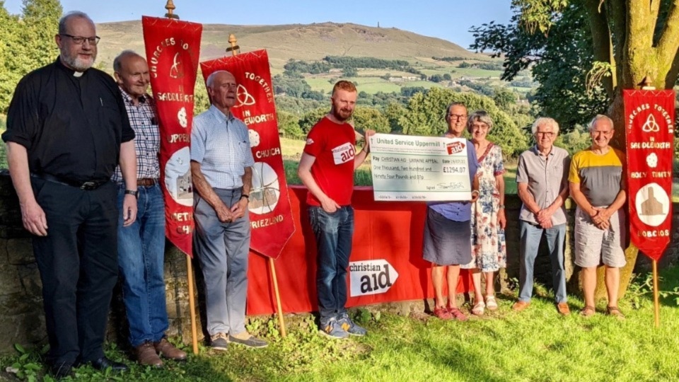 Our picture - courtesy of Beverley Wooding - shows Reverend Canon Sharon Jones, Rector of the Benefice of Saddleworth, accompanied by members of the churches, handing over the cheque to Darren Staunton from Christian Aid on behalf of the eight churches: Saint Chad Saddleworth, Sacred Heart & Saint William, Uppermill Methodist, Ebenezer Congregational, Christ Church Friezland, Saint Anne Lydgate, Kilngreen Mission and Holy Trinity Dobcross