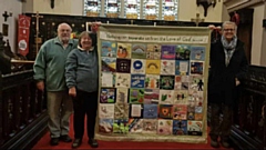 Janet is pictured with the banner, her husband Geoff and Canon Jones