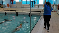 Isaac is pictured in the pool as his swimming teacher, Jordanne Alston, guides him